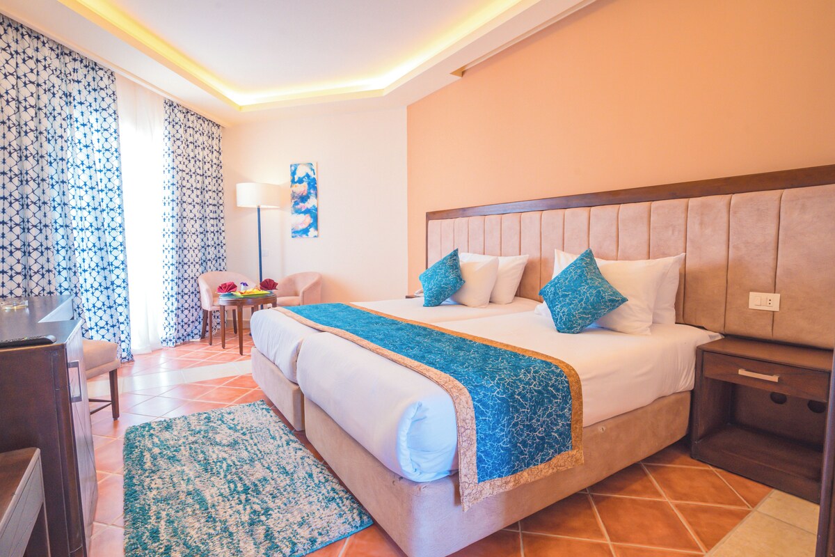 A hotel room with a large bed, a desk, a chair, and a lamp.
