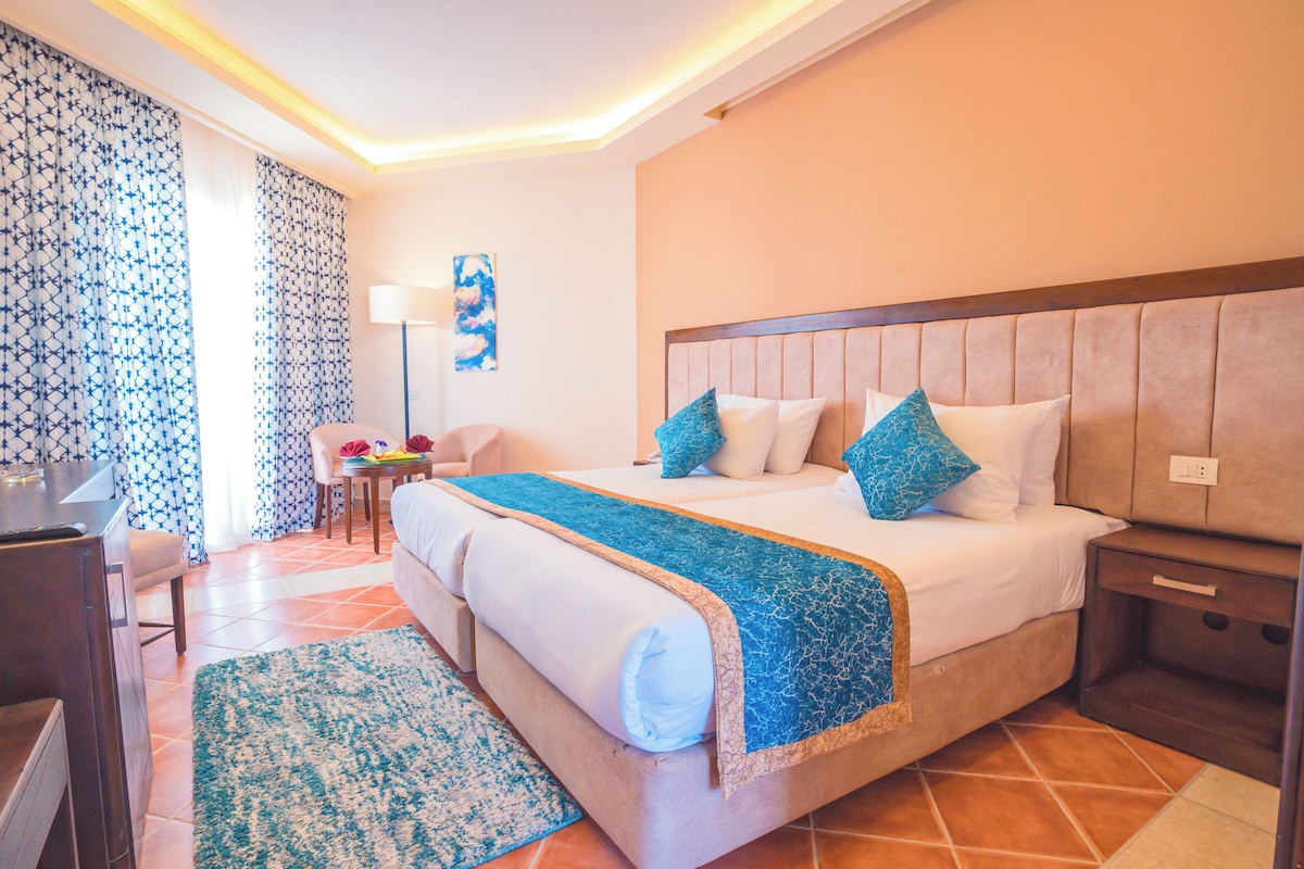 A hotel room with a large bed, a desk, a chair, and a lamp.