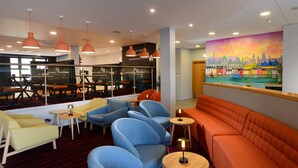 A modern lounge area with seating arrangements, pendant lighting, and a cityscape mural on the wall. - Travelodge Galway (Galway)