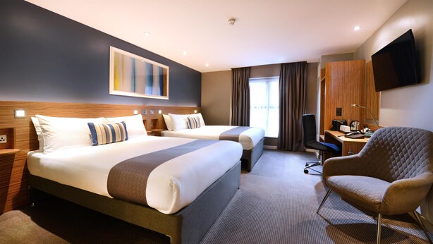 A hotel room with two beds, a desk, a chair, a TV, and a window with curtains. - Travelodge Galway (Galway)