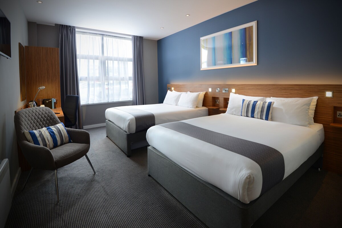 Habitación de hotel con dos camas, una zona de estar y un gran ventanal.