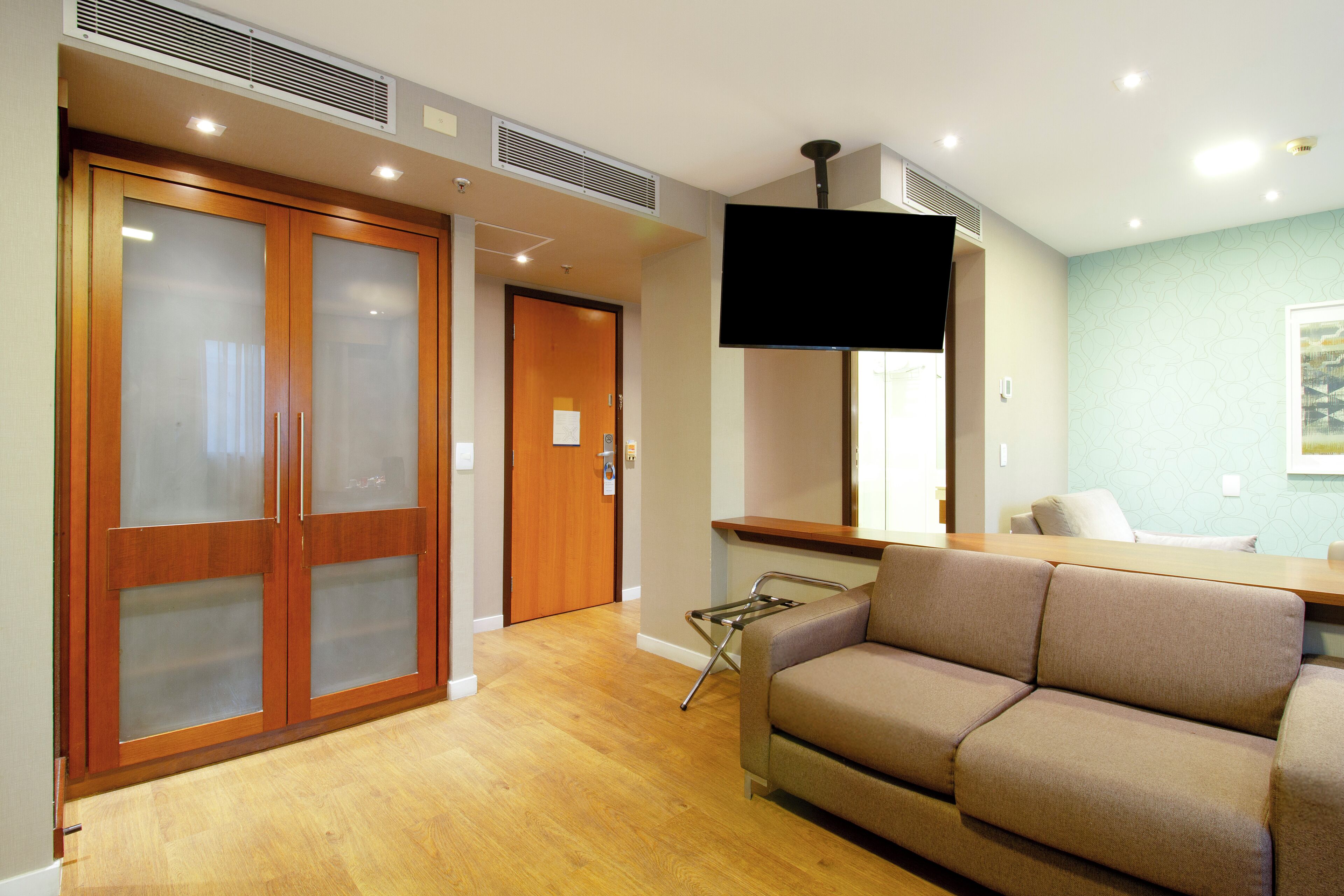 Una habitación de hotel con un armario de madera, un sofá, un televisor y una mesita.