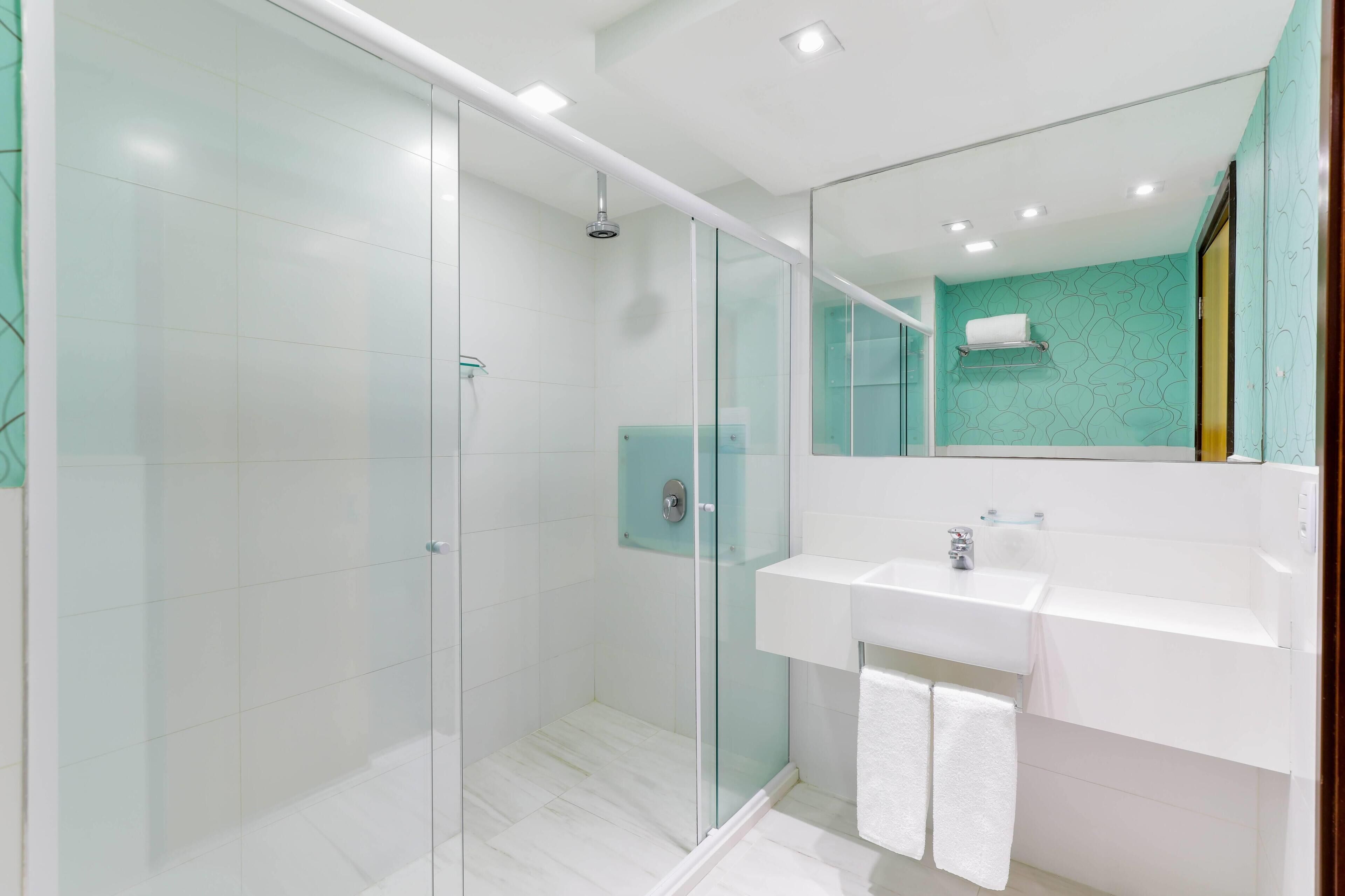 Een moderne badkamer met een douchecabine van glas, een witte wastafel en een spiegel.