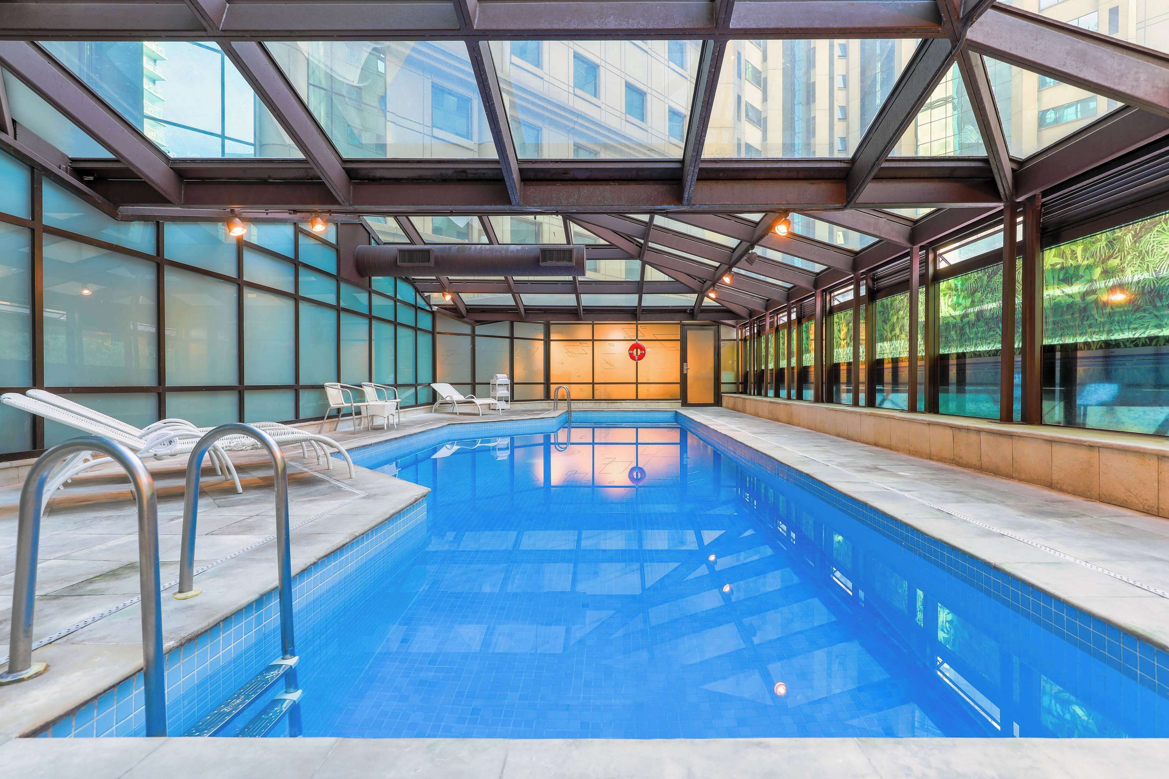 Piscina interna com paredes de vidro transparente, espreguiçadeiras e design arquitetônico moderno.