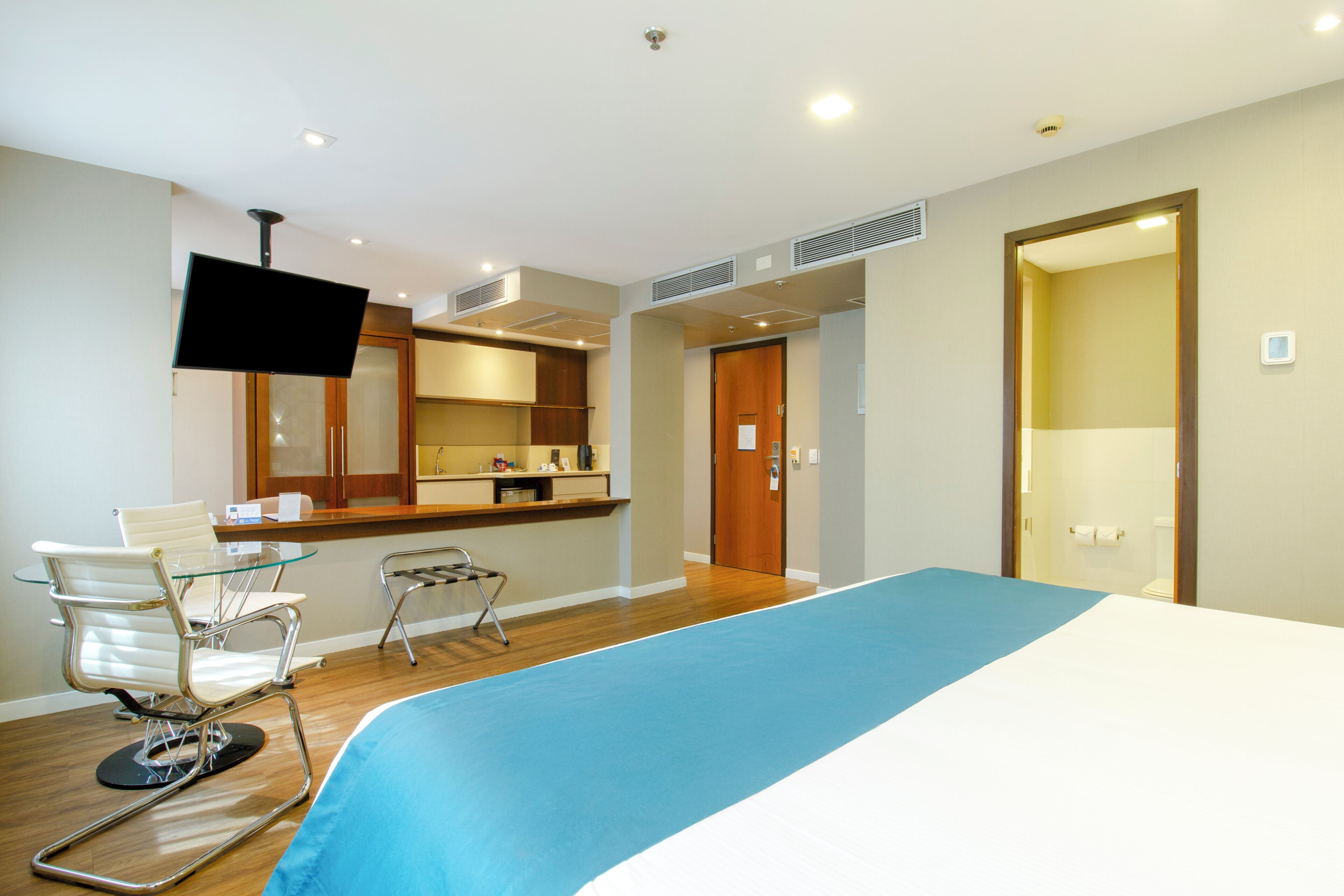 Habitación de hotel con cama, escritorio con silla, televisor y baño visible a través de una puerta abierta.