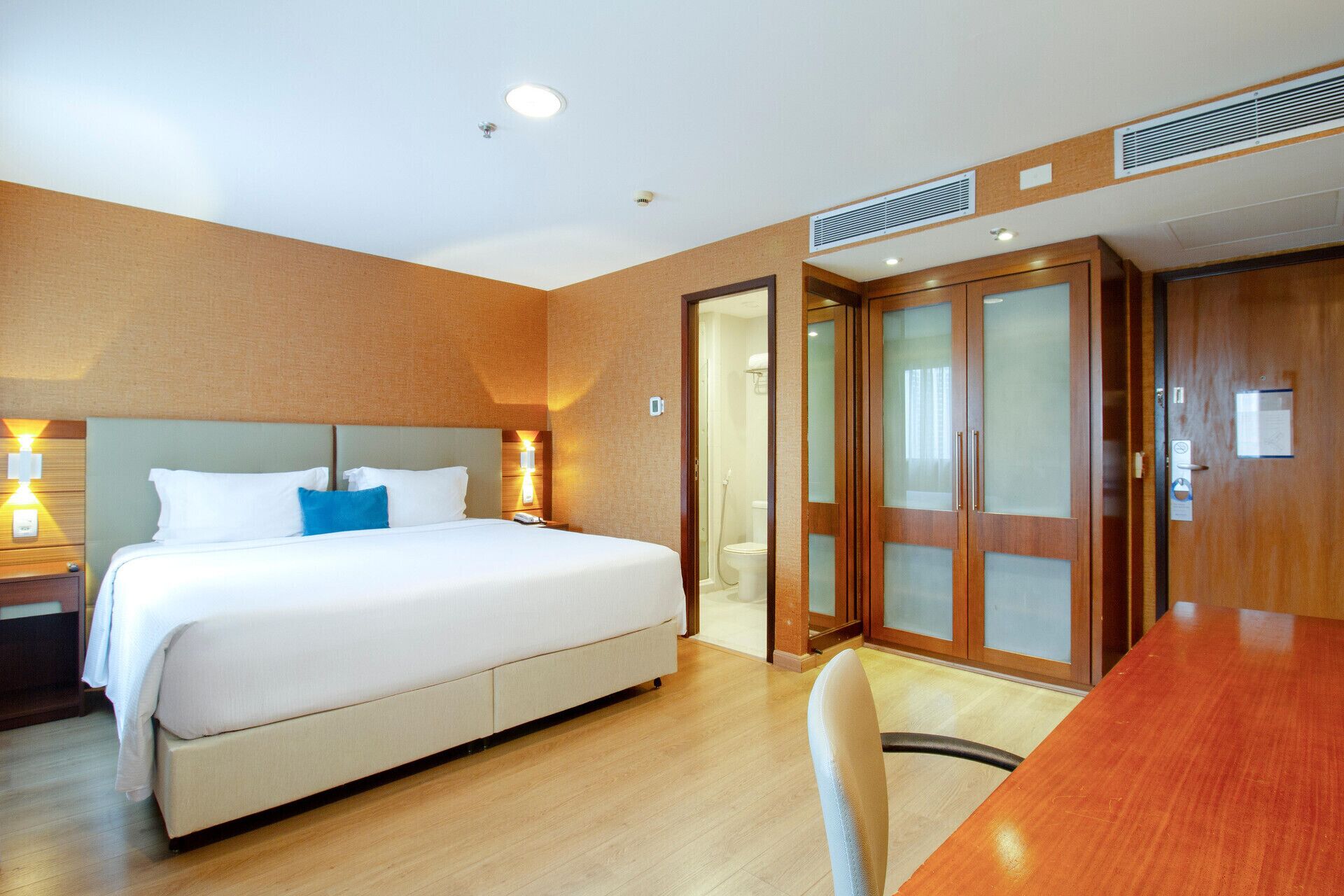 A hotel room with a bed, bedside lamps, a wooden desk, and a door leading to a bathroom.