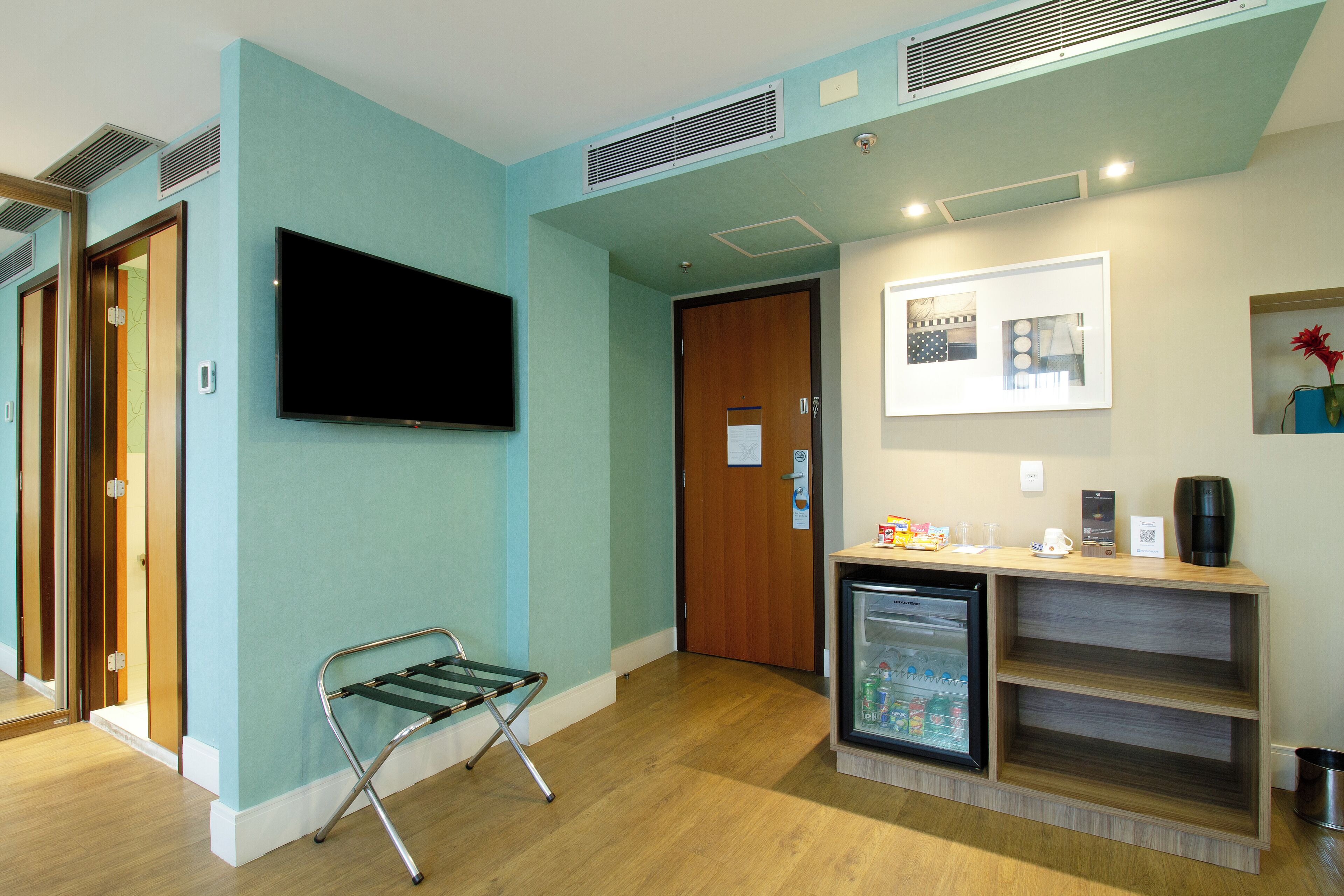 Habitación de hotel con televisión, refrigerador, puerta de madera y espejo.