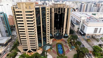 Um edifício alto com design arquitetônico moderno, apresentando um pátio central com um elemento aquático geométrico e áreas verdes ao redor.