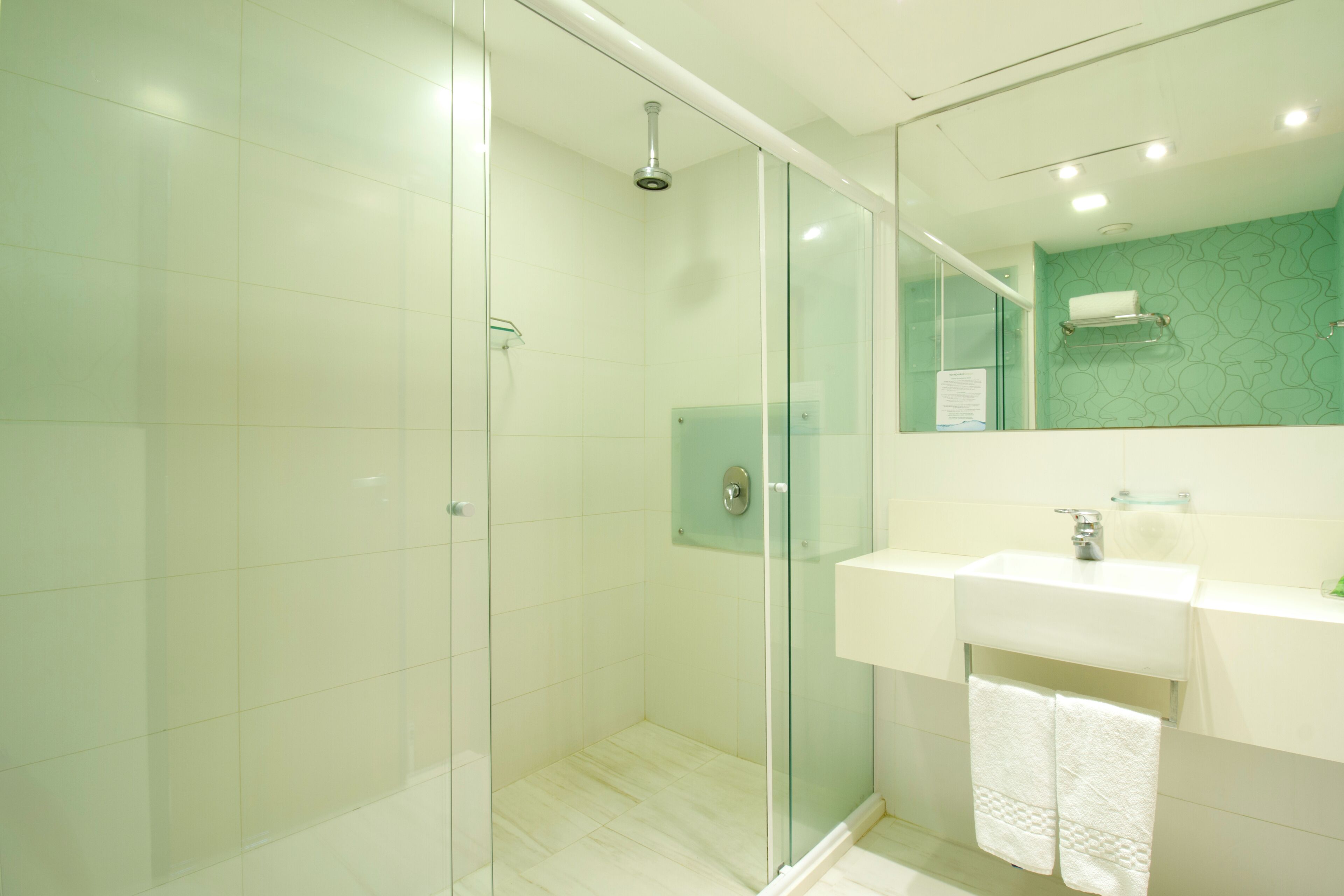 A modern bathroom with a glass-enclosed shower, a white sink, and a mirror with a green-tiled wall.