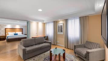 Quarto de hotel com uma cama, dois sofás, uma mesa de vidro e um tapete estampado.