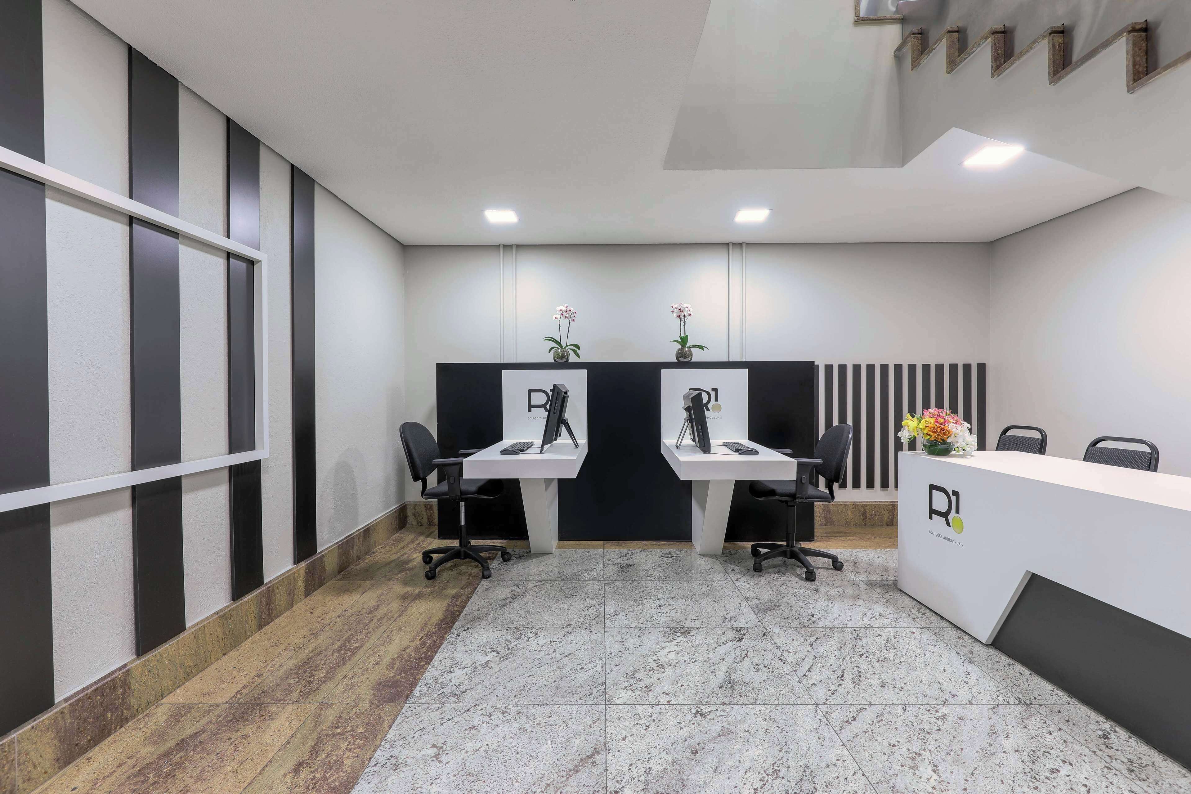 Uma área de recepção de escritório moderna com duas mesas, cadeiras e um balcão de atendimento com um logotipo.