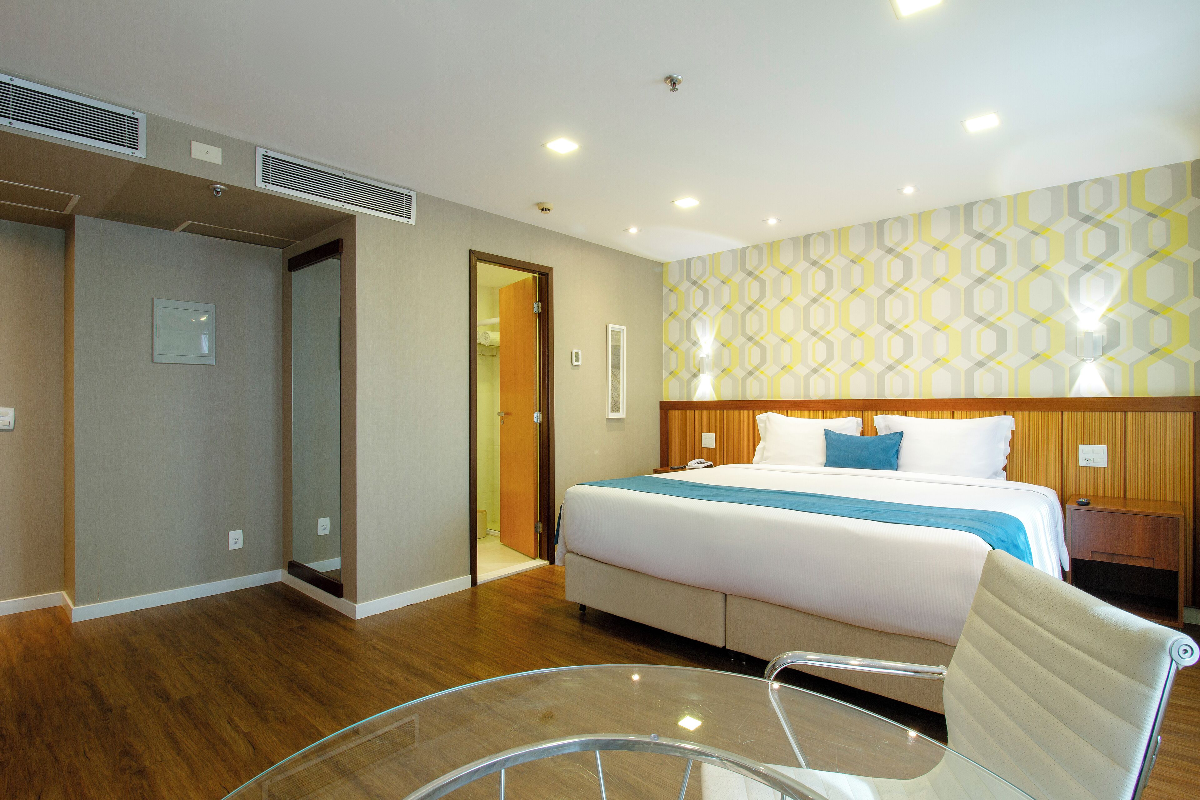 A hotel room with a bed, bedside table, chair, and a mirror.