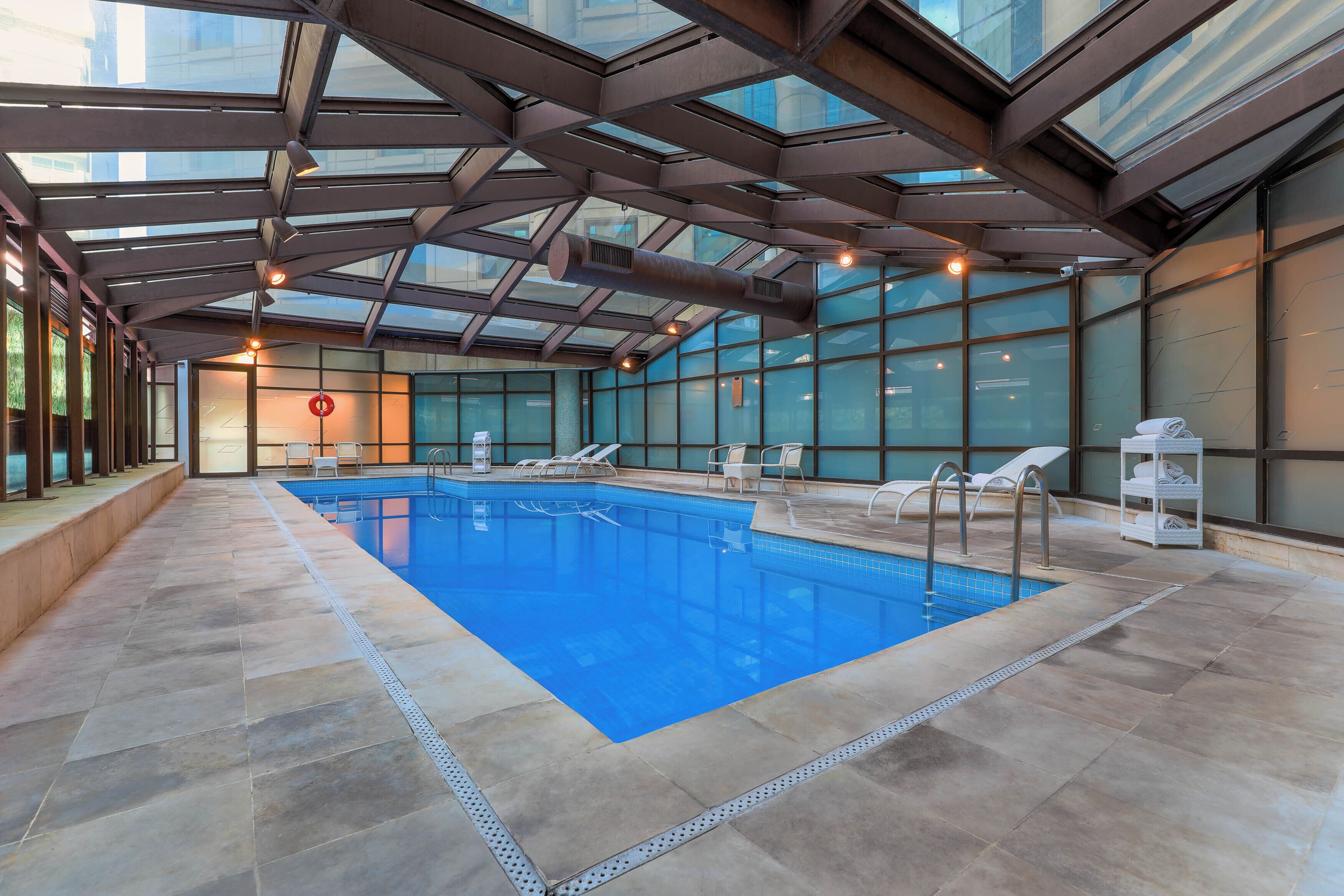An indoor swimming pool with clear blue water, surrounded by lounge chairs and a glass ceiling.