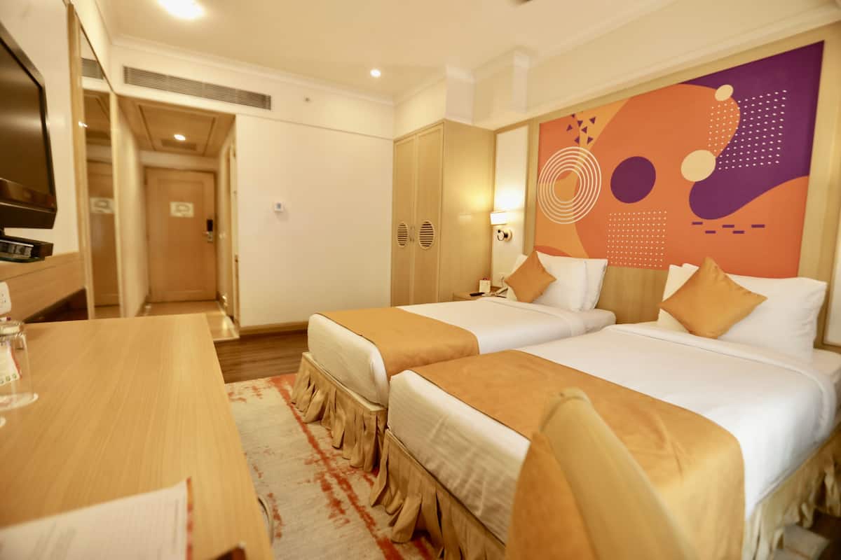 Une chambre d’hôtel avec deux lits, un bureau en bois, une télévision et un mur décoratif.