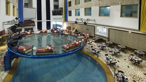 A large indoor swimming pool with a glass barrier, surrounded by tables and chairs for dining.