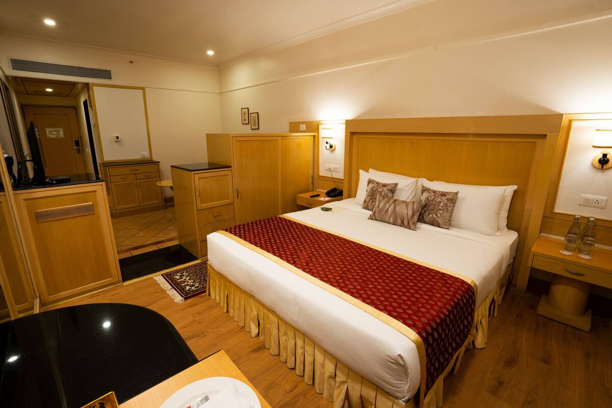Une chambre d’hôtel avec un grand lit, une tête de lit en bois, des tables de chevet, un bureau et une armoire.