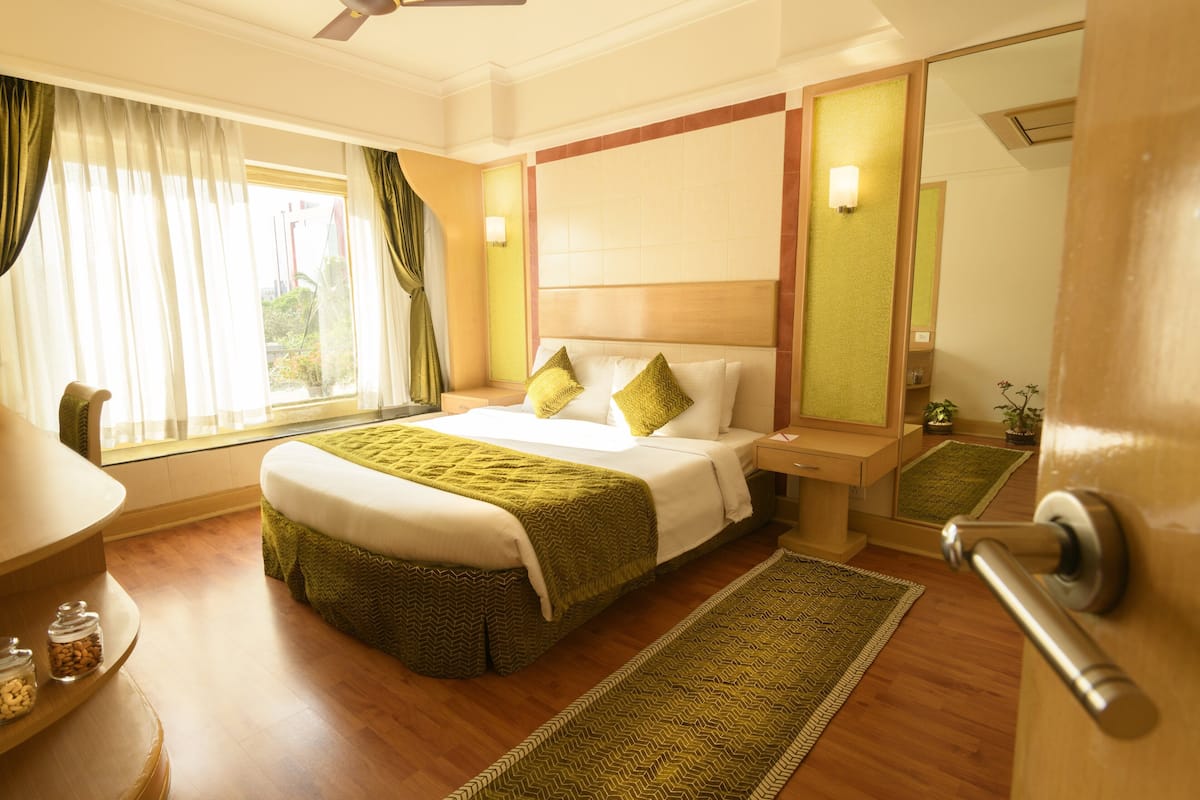 Une chambre d’hôtel avec un grand lit, une table de chevet, un miroir et une fenêtre avec des rideaux.