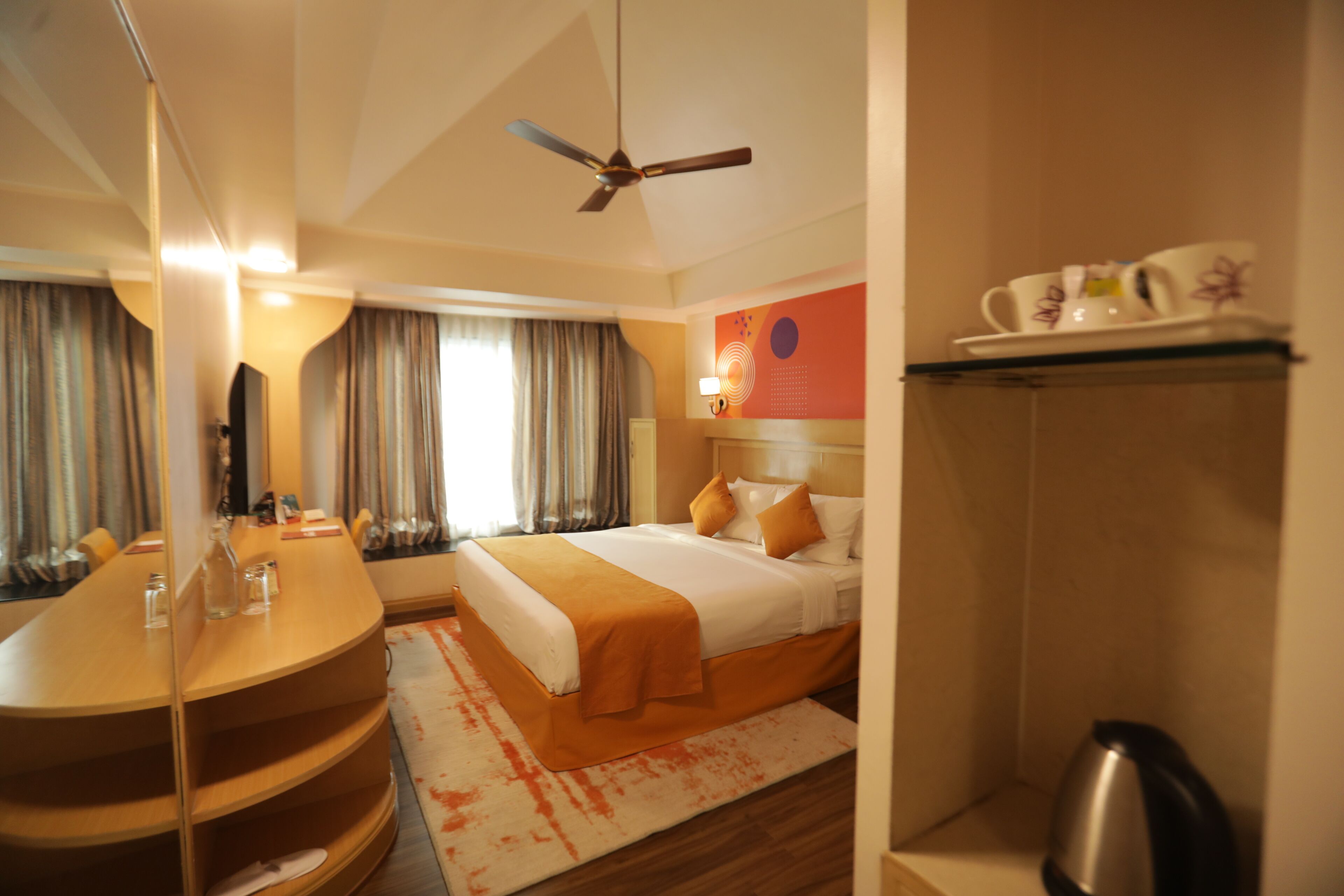 Een hotelkamer met een bed, bureau, spiegel, plafondventilator en een douche.