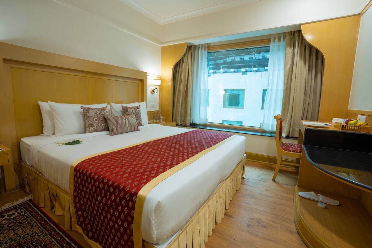 Une chambre d’hôtel avec un grand lit, une télévision, une fenêtre avec des rideaux et une tête de lit en bois.