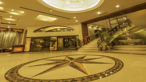 A spacious lobby with a central geometric floor design, a grand staircase, and a large circular skylight.