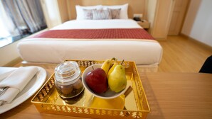 A hotel room with a neatly made bed, a tray with fruits and a jar of jam on a table.