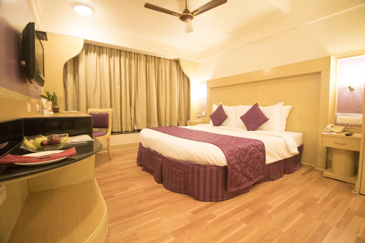 Une chambre d’hôtel équipée d’un lit, d’un bureau avec un ordinateur, d’une chaise, d’une télévision et d’un ventilateur de plafond.