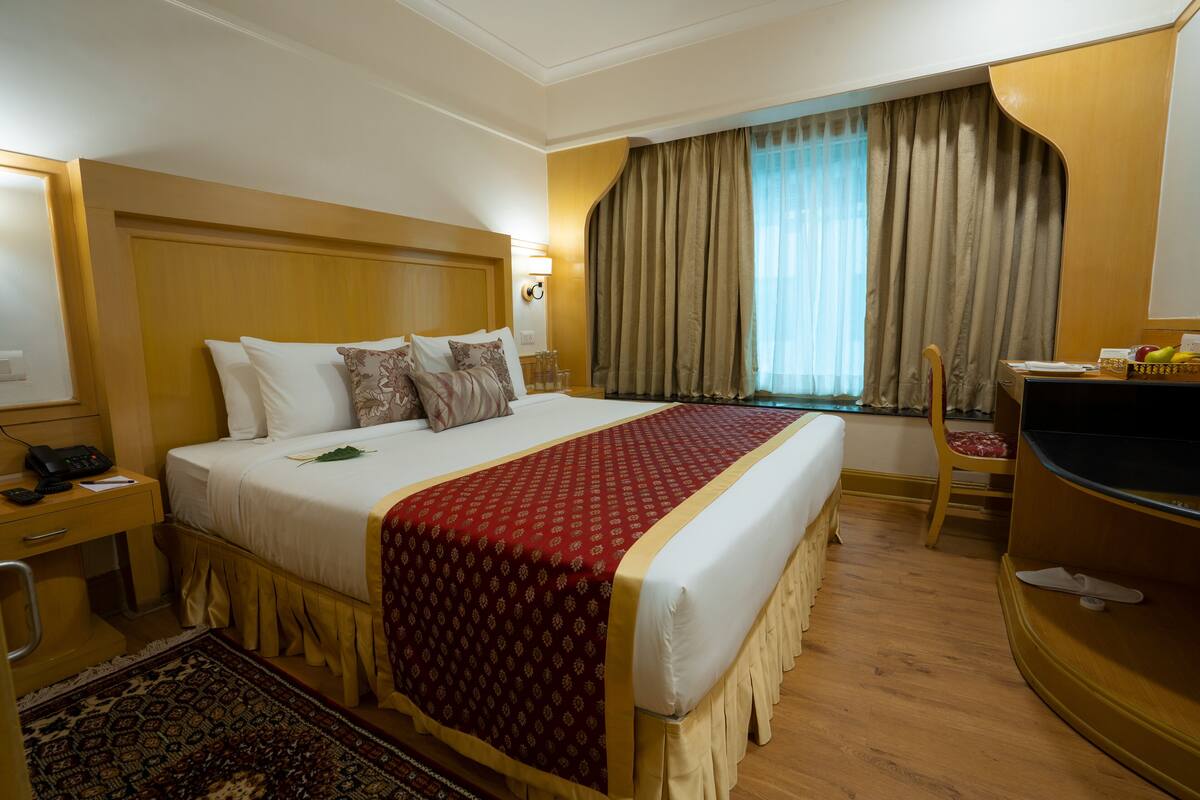 Une chambre d’hôtel avec un grand lit, un bureau, une chaise, une télévision et une fenêtre avec des rideaux.