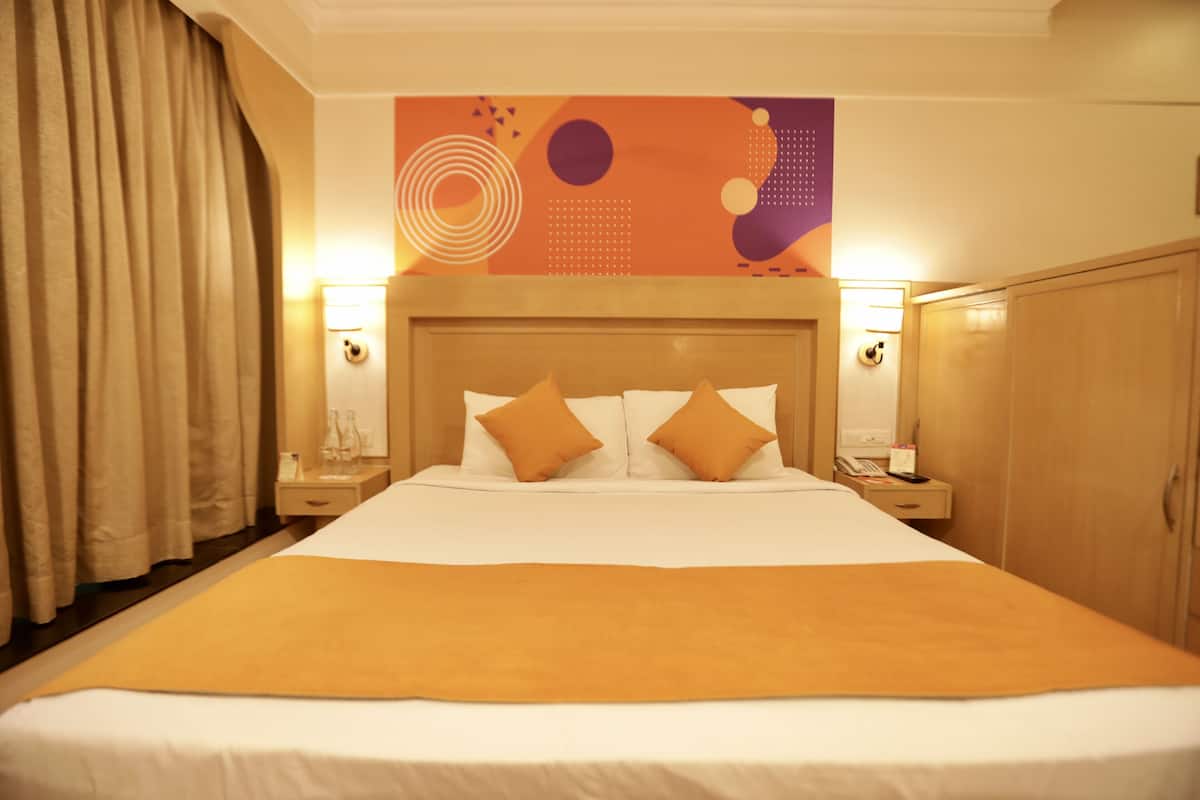 Une chambre d’hôtel avec un grand lit, deux tables de chevet, une armoire en bois et une décoration murale abstraite et colorée.