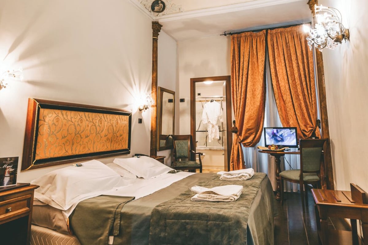 Habitación de hotel con cama, escritorio, silla, televisor y espejo.