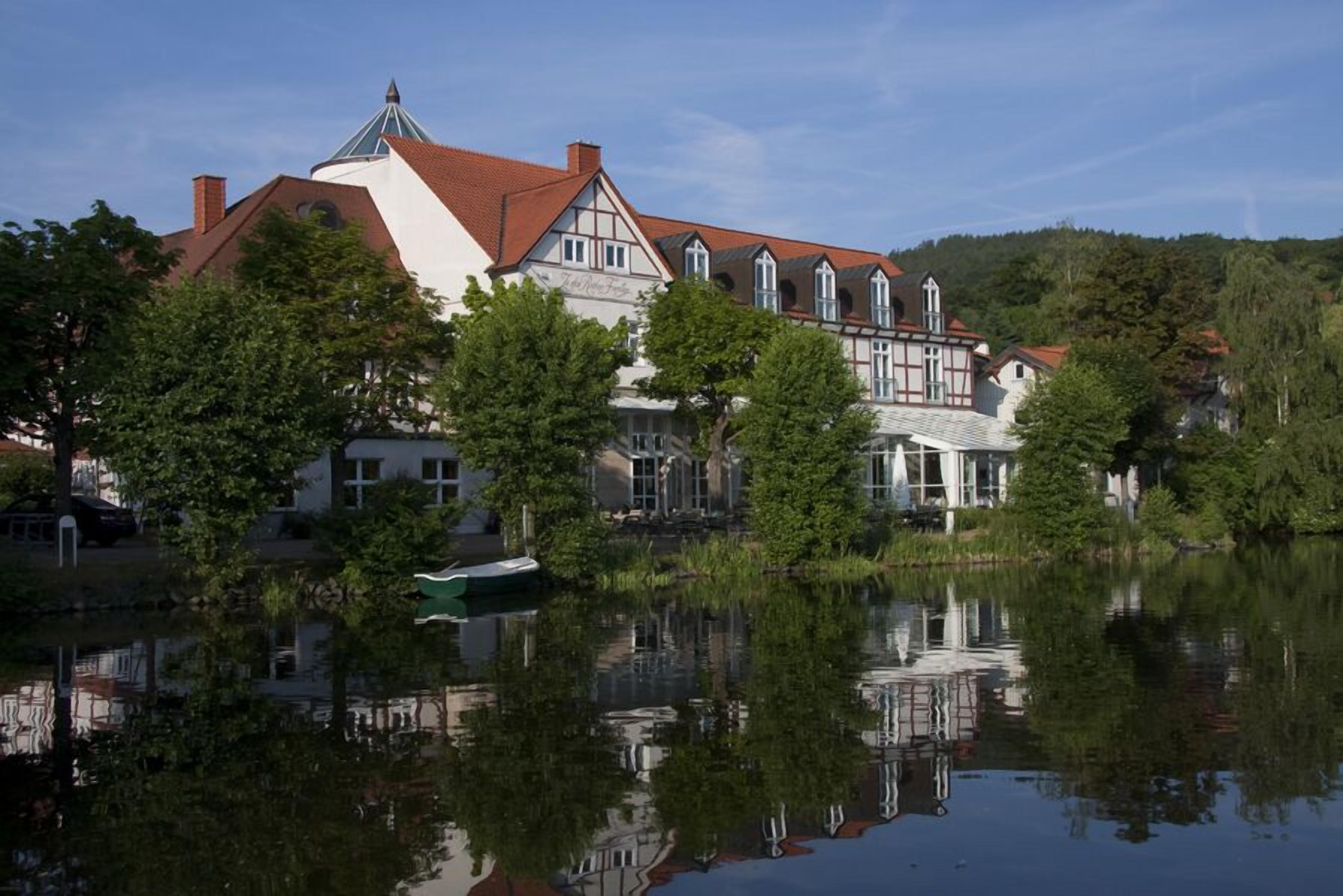 Un grand bâtiment historique, doté d’une tour imposante et de nombreuses fenêtres, situé au bord d’un lac paisible dont les eaux reflètent le paysage.