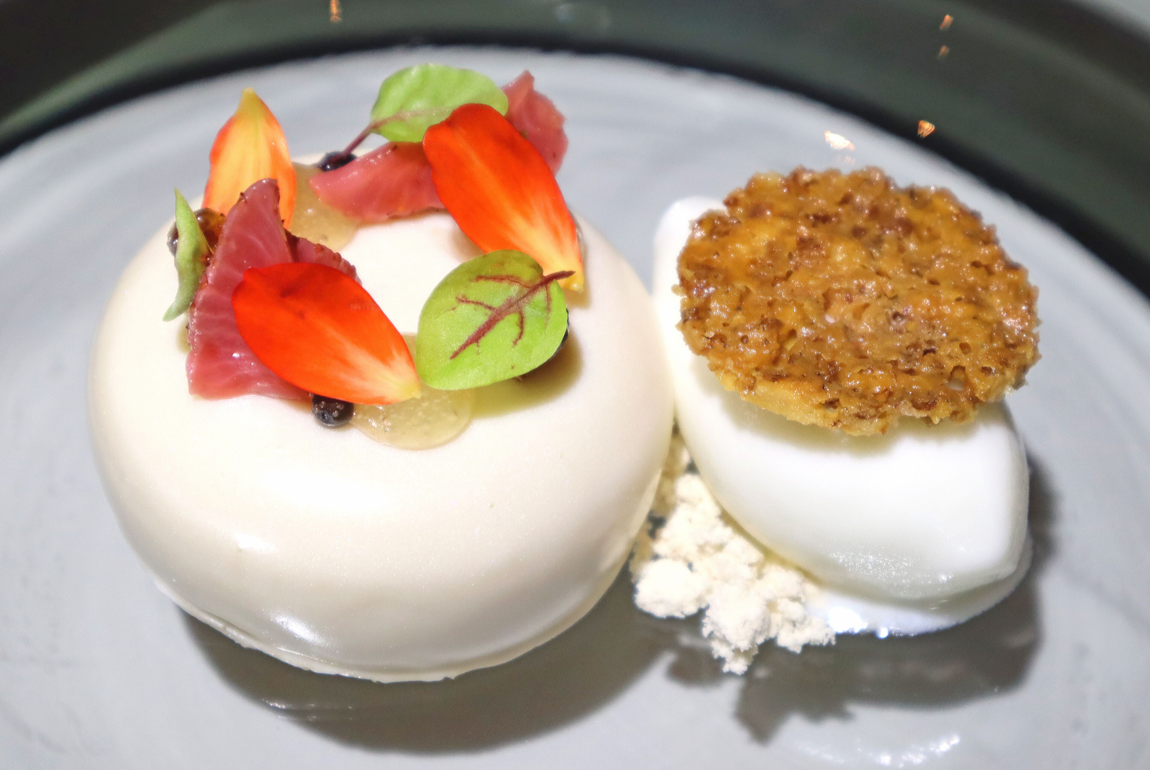 A dessert with a smooth white base, topped with vibrant red and green leaves, and a golden-brown crispy element.