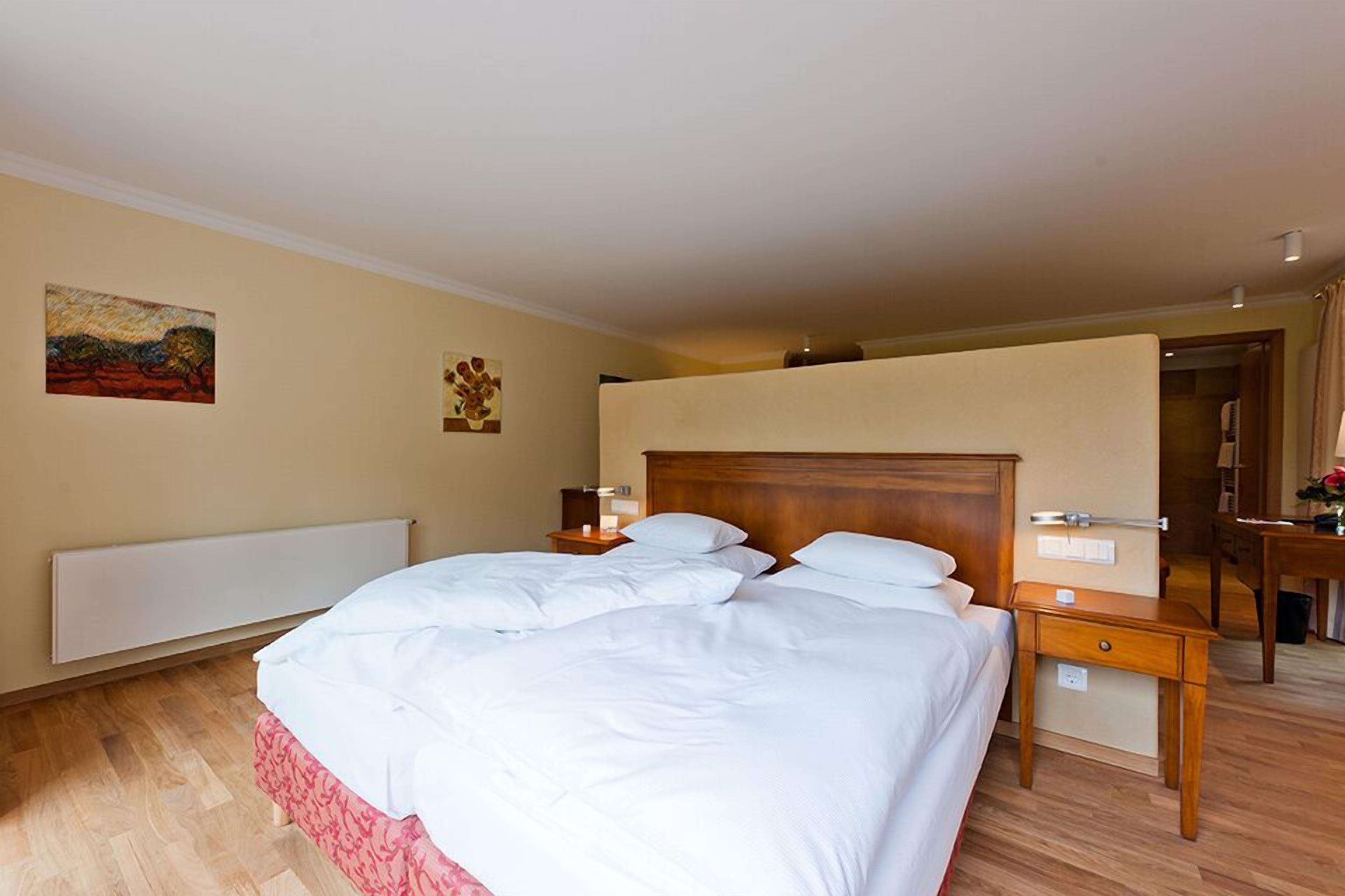 A hotel room with a large bed, a wooden headboard, a bedside table, a nightstand, and a mirror.