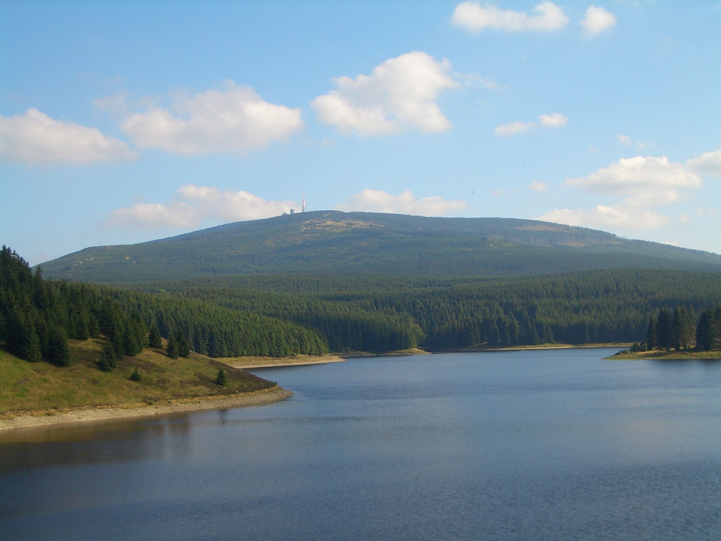Un lac entouré d’une forêt dense et une colline surmontée d’une tour.