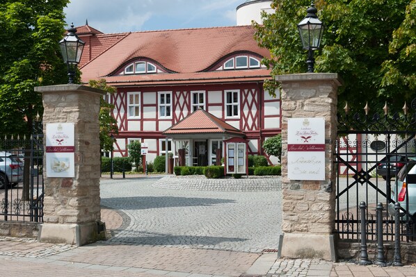 Un edificio tradicional con entramado de madera, una entrada adoquinada, pilares de piedra con letreros y una puerta de metal.