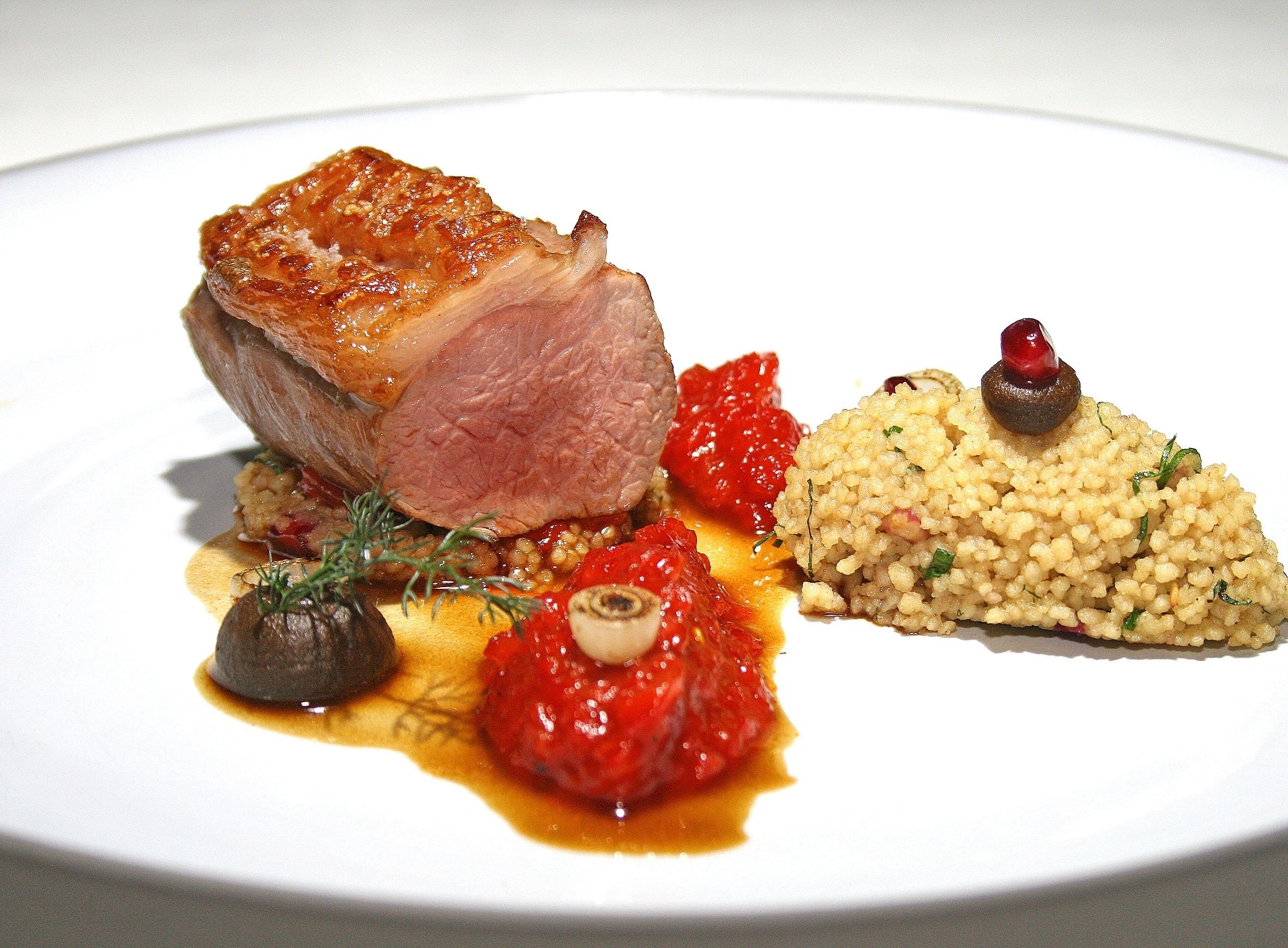 A plated dish with a piece of meat, vegetables, and a grain-based side.