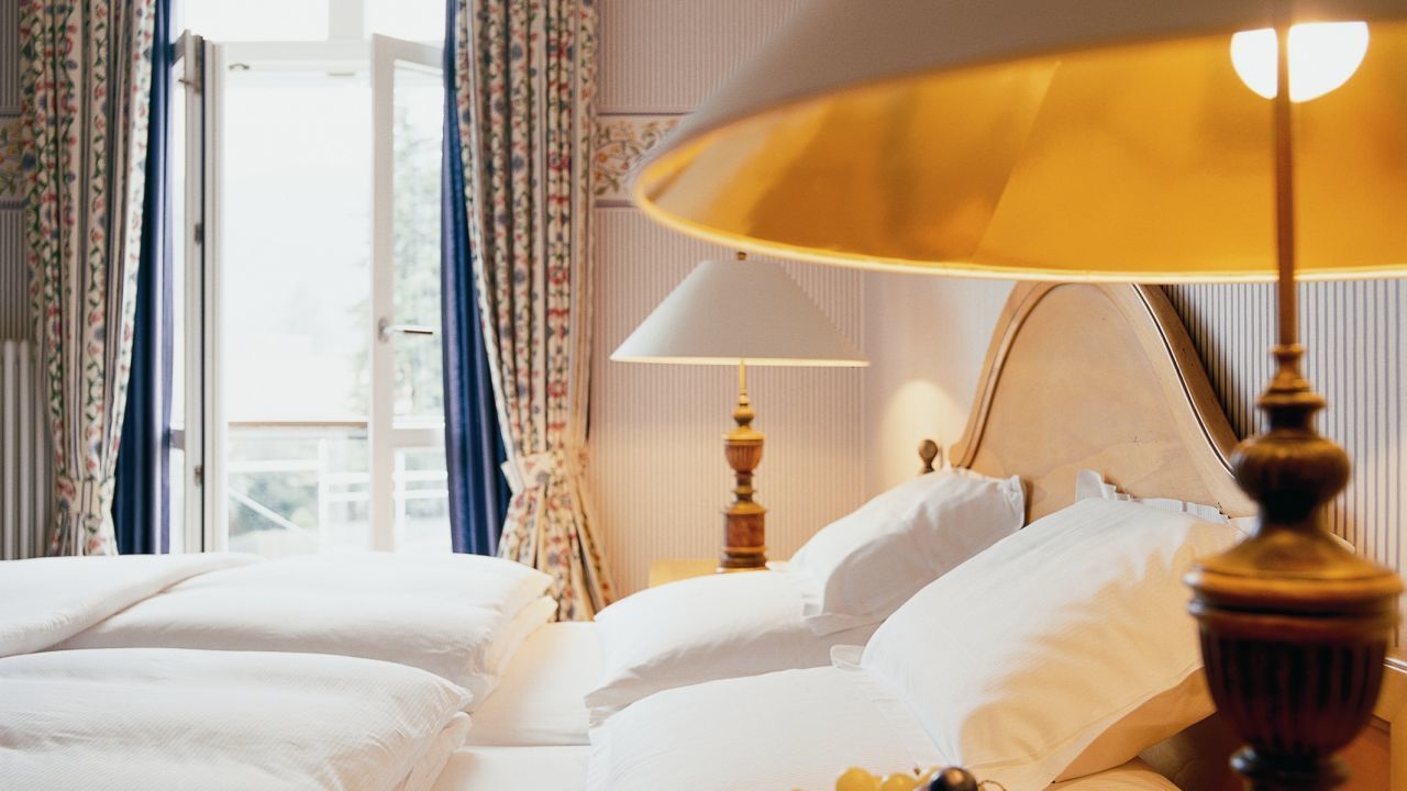 A hotel room with a bed, a lamp, and curtains.