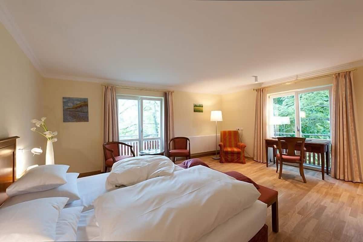 Une chambre d’hôtel avec un grand lit, deux chaises, un bureau et une fenêtre avec des rideaux.
