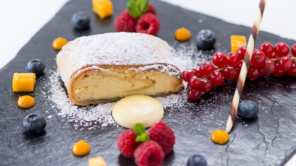 A dessert with a dusting of powdered sugar, surrounded by various berries and a small dollop of cream.
