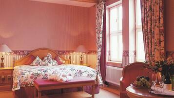 Una camera da letto con un letto di legno, un comodino, una sedia e una finestra con tende floreali.