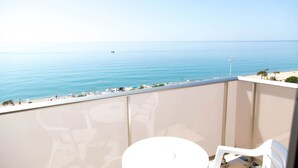 Een balkon met uitzicht op zee, een witte tafel en witte stoelen.