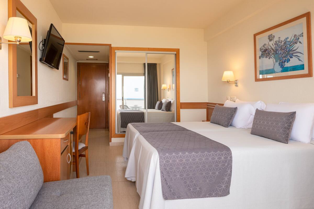 Habitación de hotel con cama, escritorio, silla, televisor y un cuadro en la pared.