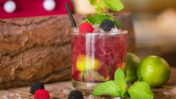 A glass of iced beverage with berries and mint, surrounded by ice cubes and lime on a wooden surface.