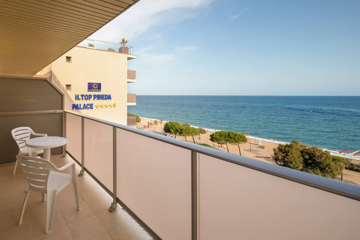 Un balcón con vista al mar, un cartel de H. Top Pineda Palace y dos sillas de plástico blancas.