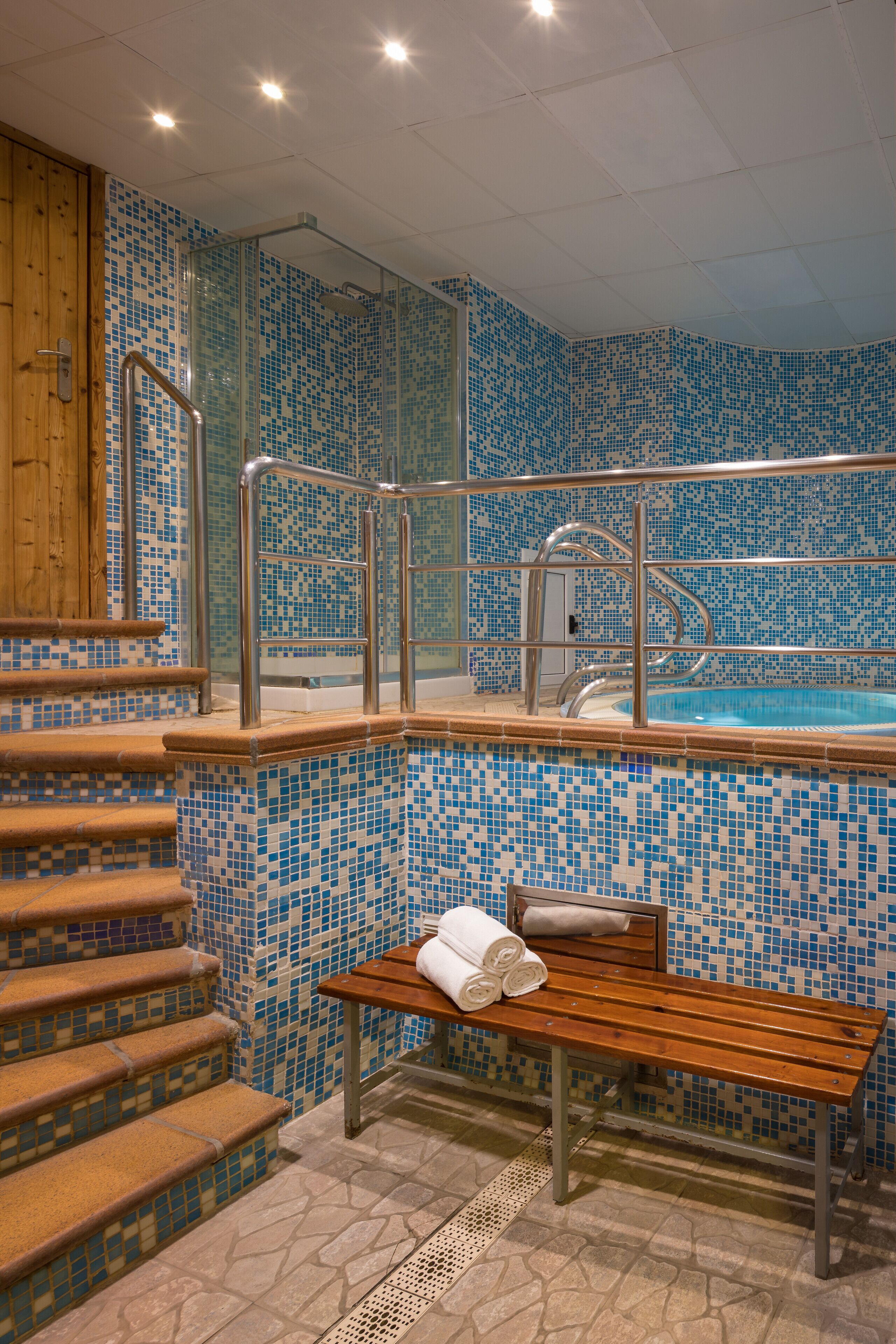 Une salle de bain avec un mur carrelé, un banc et une piscine.