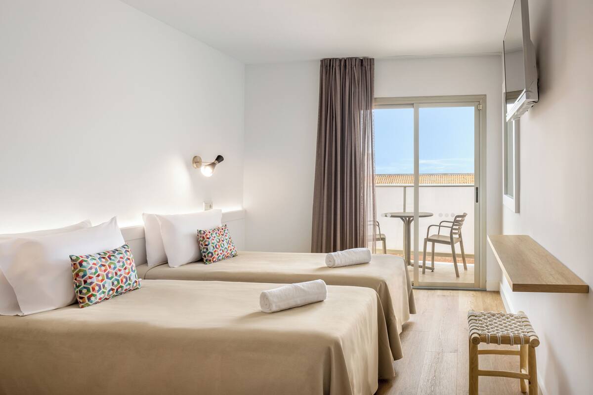 Habitación de hotel con dos camas, una mesita, una silla, televisor y balcón con vistas.