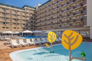 A hotel pool area with sun loungers and umbrellas, surrounded by a multi-story building with balconies.