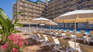 Een zwembadgedeelte van een hotel met ligbedden en parasols, omringd door een meerlaags gebouw met balkons.