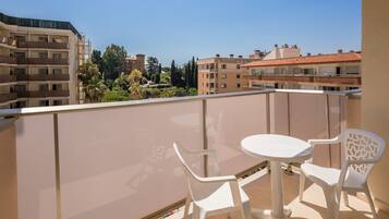 Un balcón con una mesa redonda y dos sillas blancas, con vistas a una zona residencial con varios edificios y árboles.