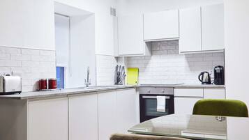 A modern kitchen with white cabinetry, a built-in oven, and a dining area with a green chair.