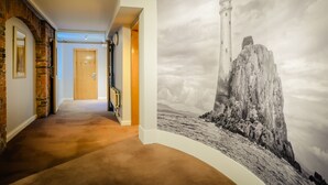 Um corredor com uma porta de madeira, parede de tijolos e um grande mural na parede com a imagem de um farol.
